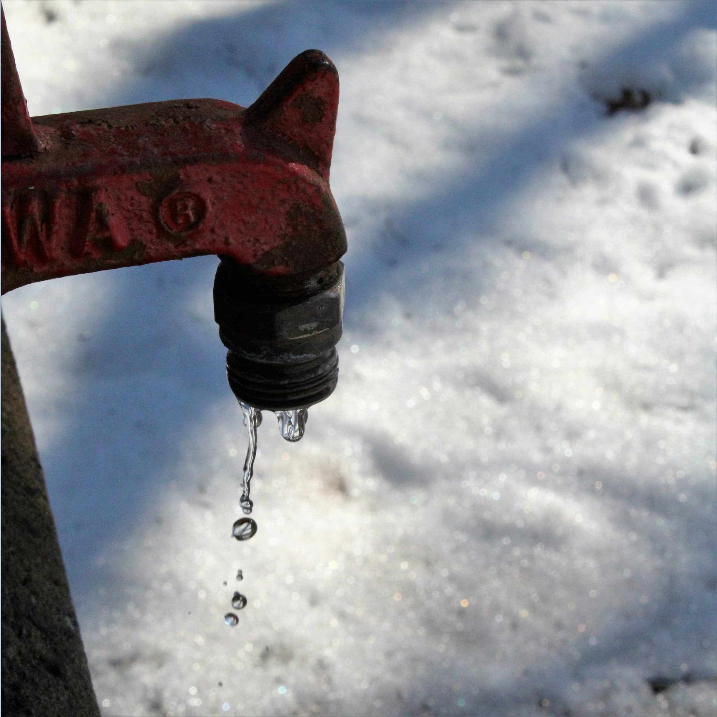 Outdoor spigot dripping over snow in freezing weather